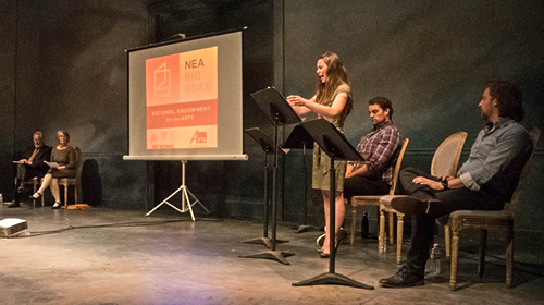 Actors stand on stage, reading from podiums.