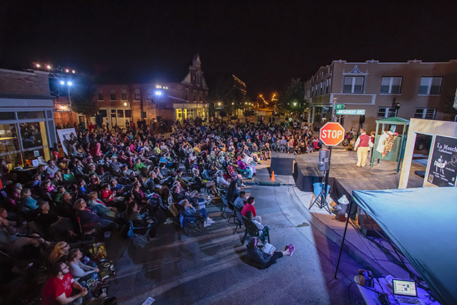 An audience watches an outdoor, nighttime performance on a stage