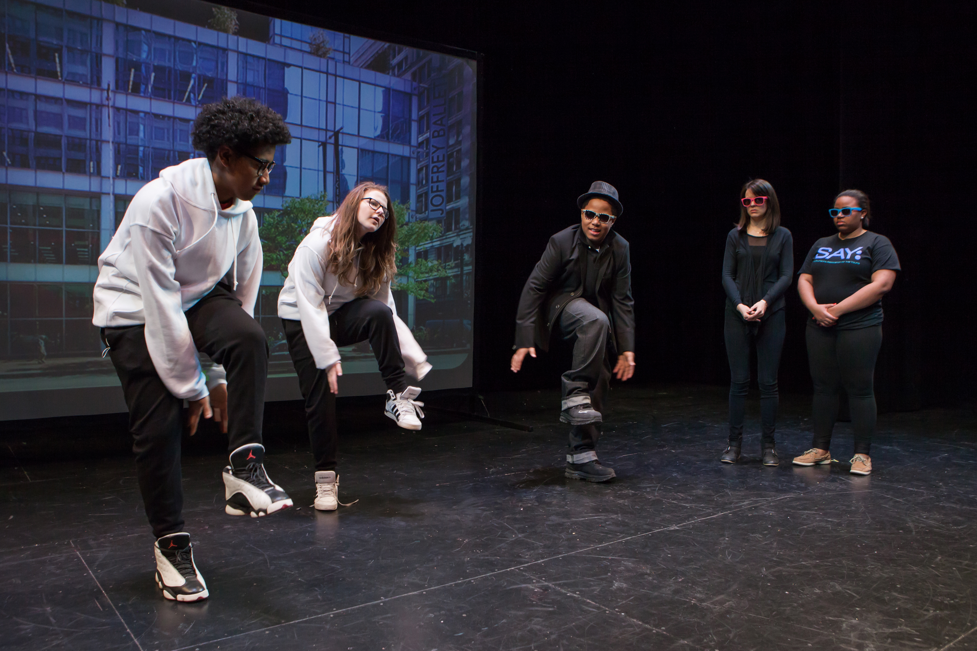 Kids dressed in sweatshirts dancing on stage. 