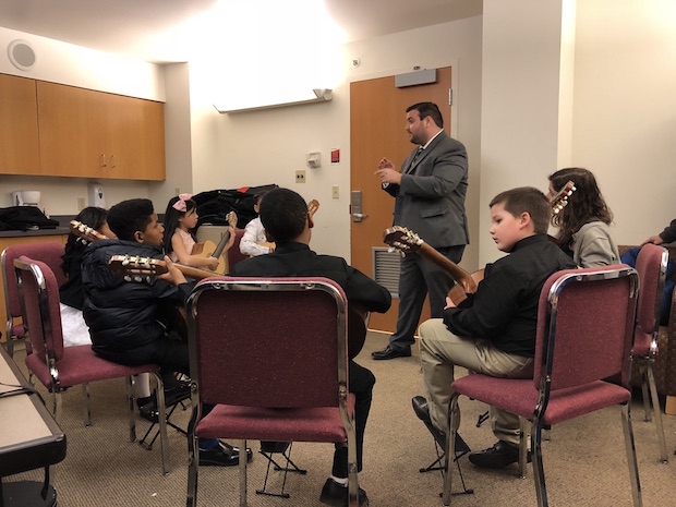 a group of young students sits in a circle with their guitars and listening to an adult