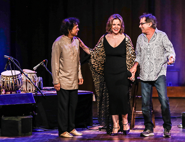 A woman flanked by two men onstage