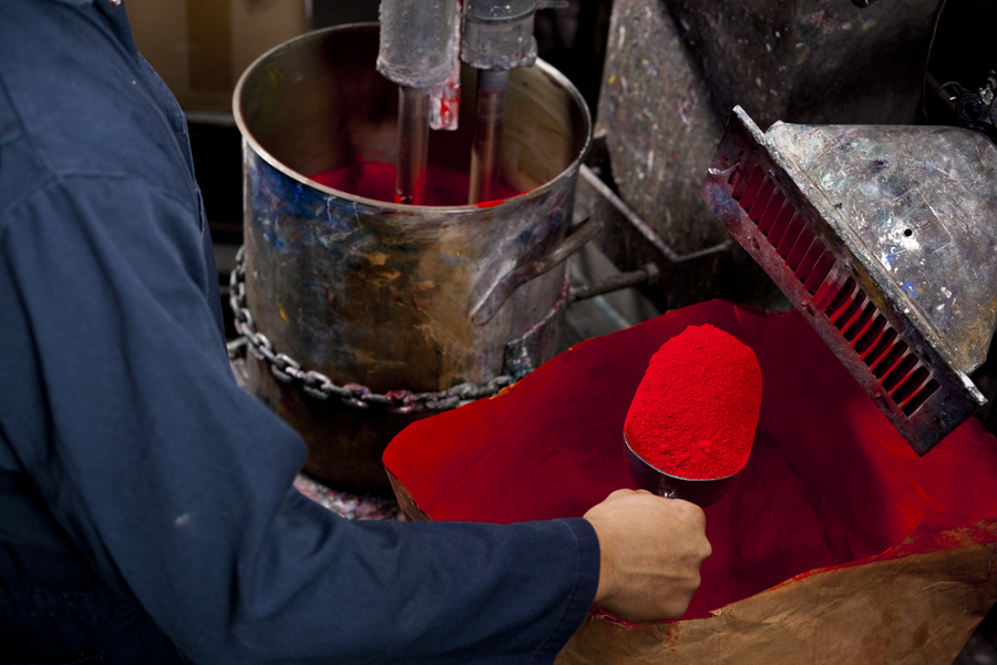 Hand of man putting shovel full of red pigment into mixer machine.