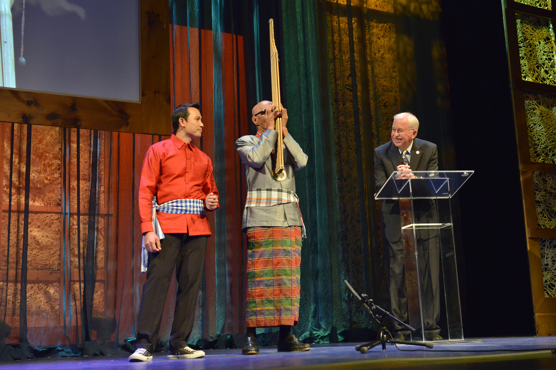 The fellow is playing a instrument while his translator stands next to him singing. 