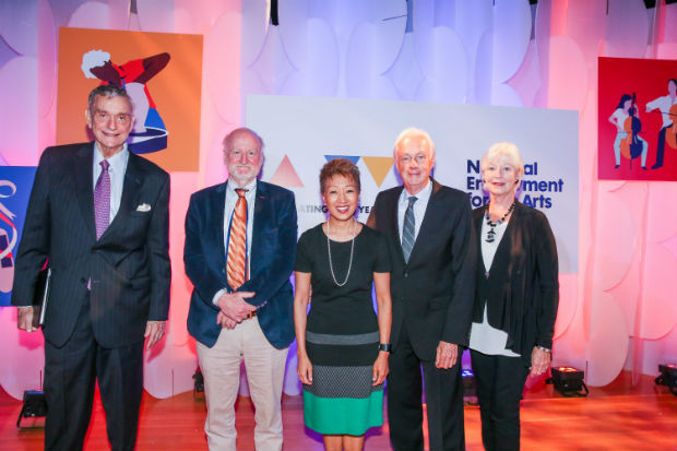 Three men stand with two women on a stage with backdrop