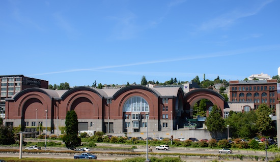 a dark red-bricked factory like space that houses the museum with a highway running in front of it