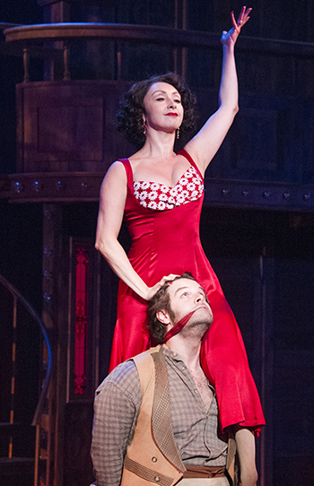 Woman in red dress raising left arm stands above man in vest