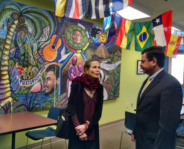 Julia Alvarez standing in front of colorful mural. Latin American flags hang from the ceiling.