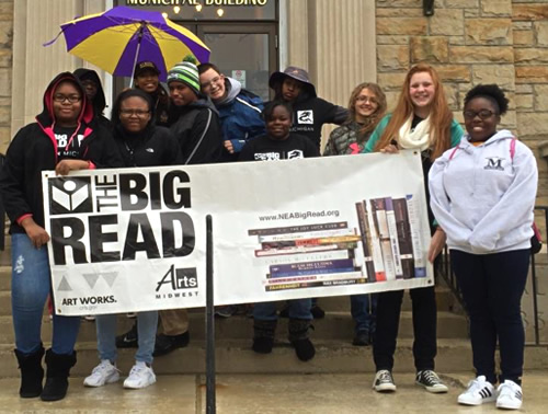 Group of students stand smiling in the rain with a Big Read banner.