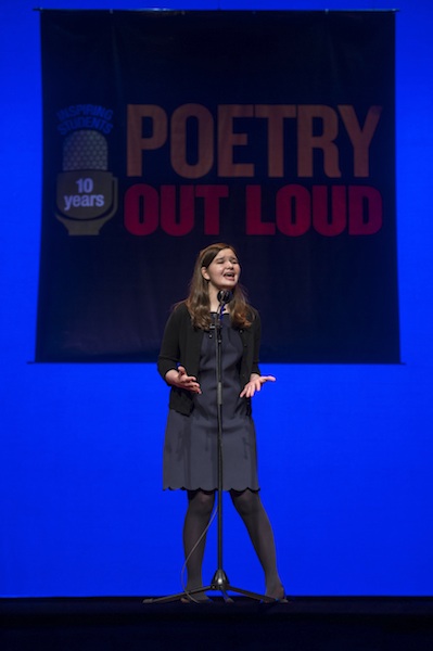 a young white woman recites a poem on stage into a microphone
