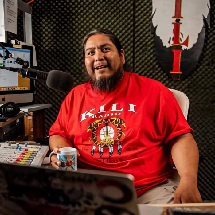 A man in a radio studio looks at the camera.