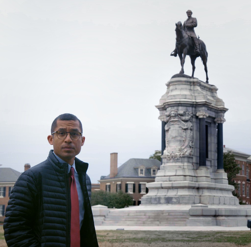 A m posing with a statute in the background.