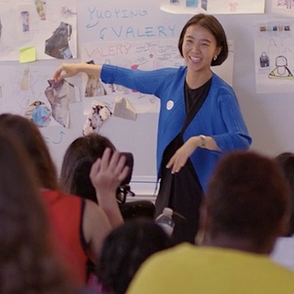 A smiling woman at the front of a class point to a picture on the wall.