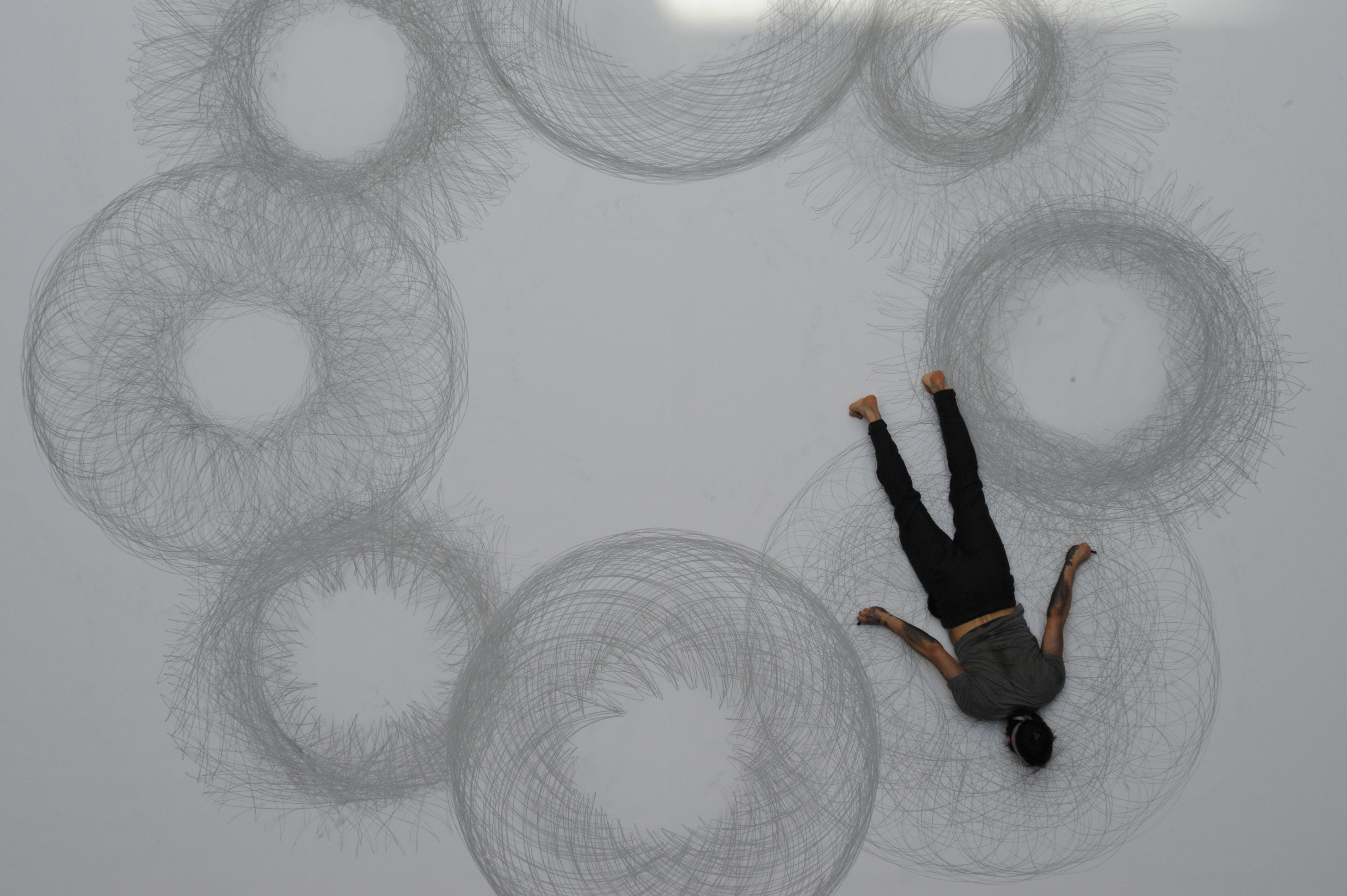 Man lying on paper with charcoal and drawing circles. 