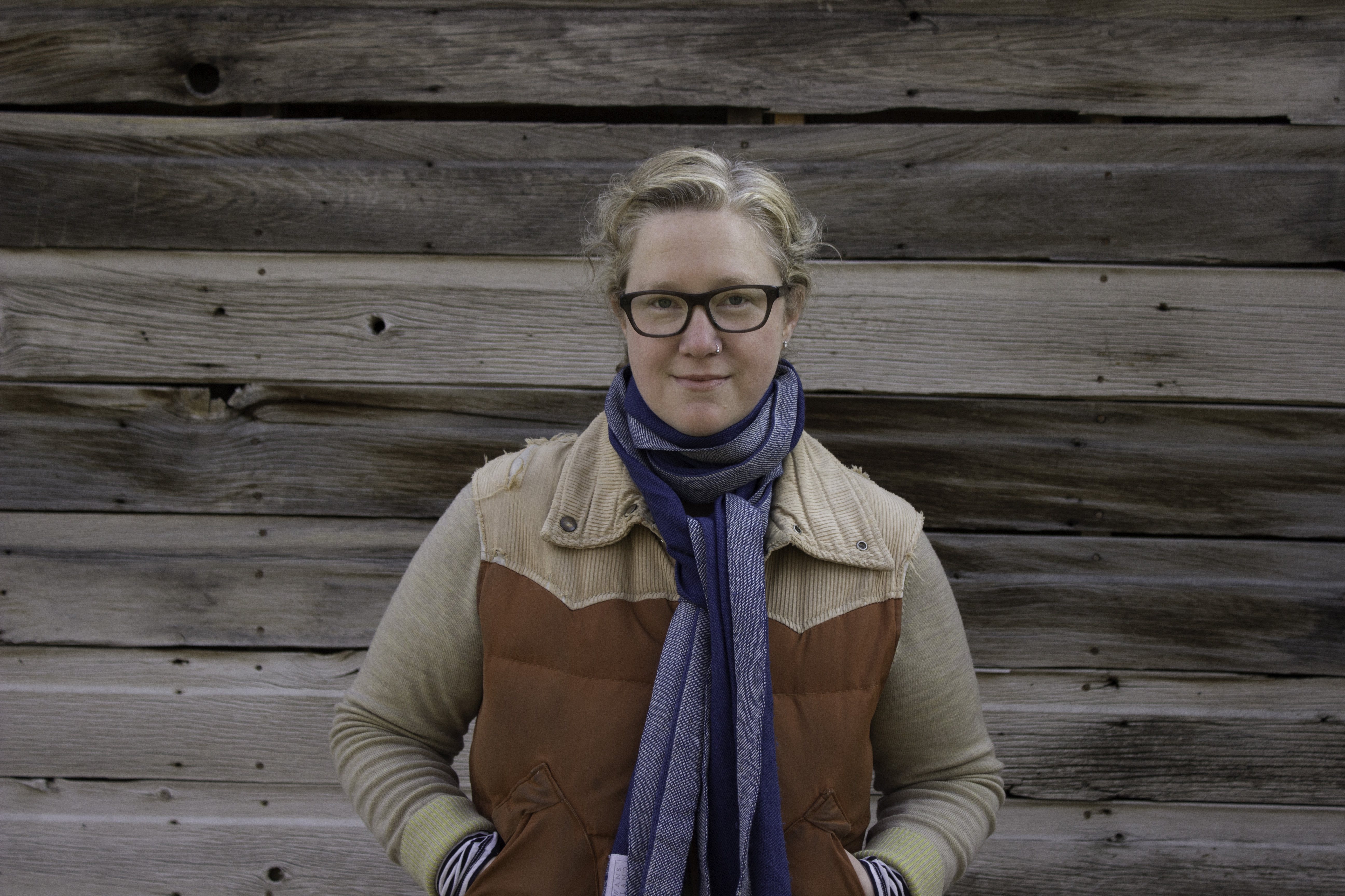 A woman with light tan jacket and a scarf poses.