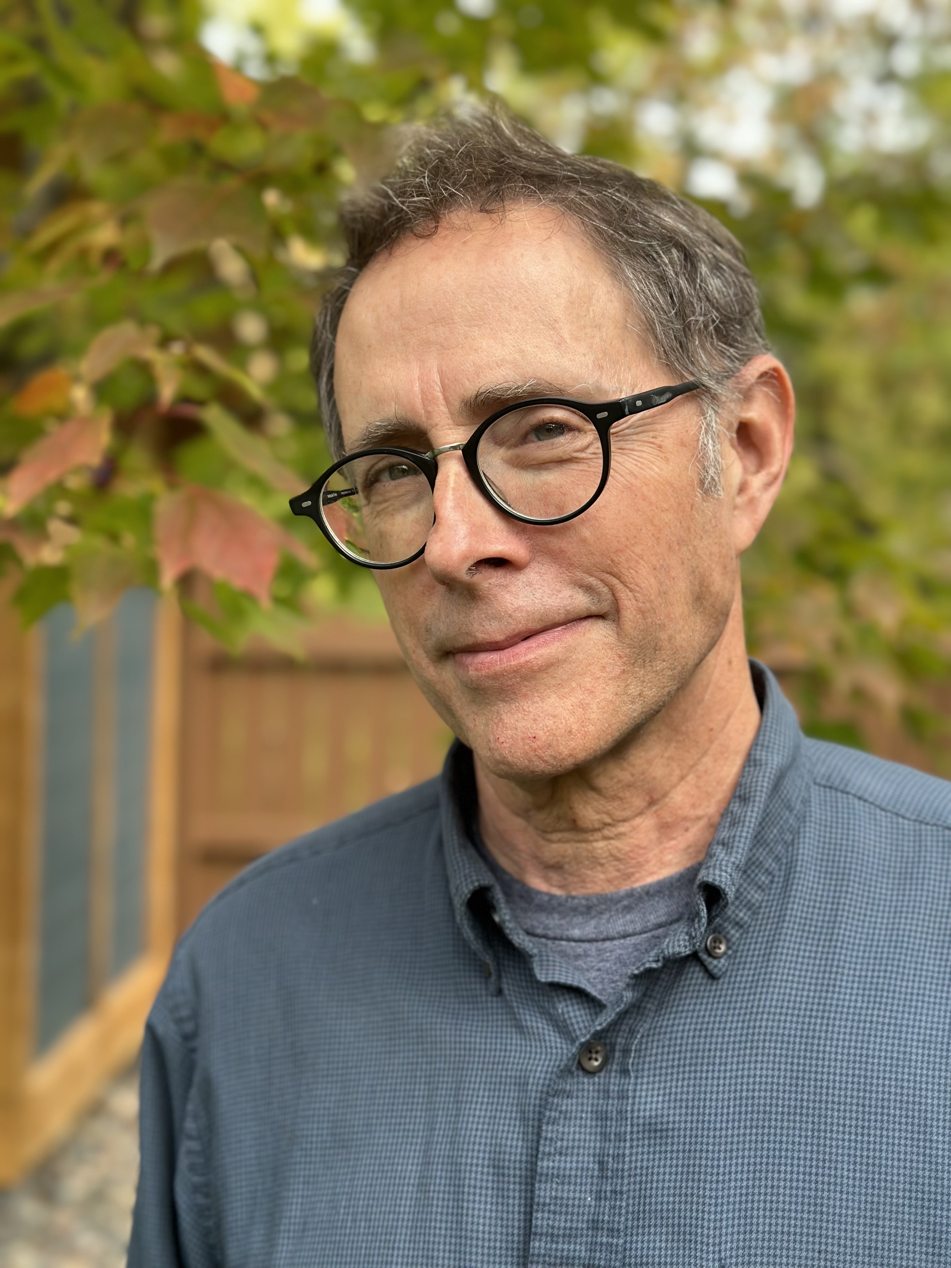 A white man with grey shirt poses in front of a tree.