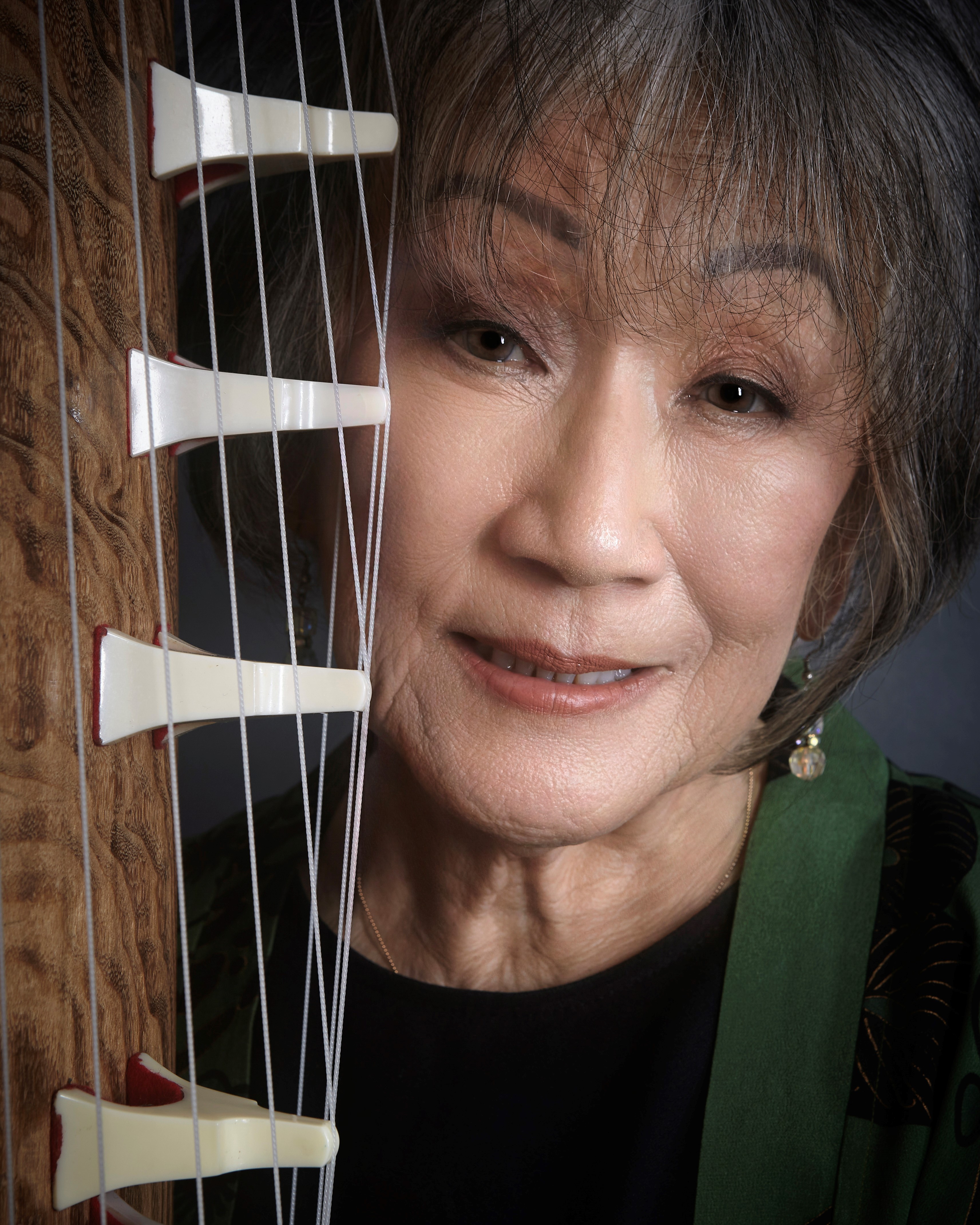 Photo of an Asian woman smiling next to a koto instrument