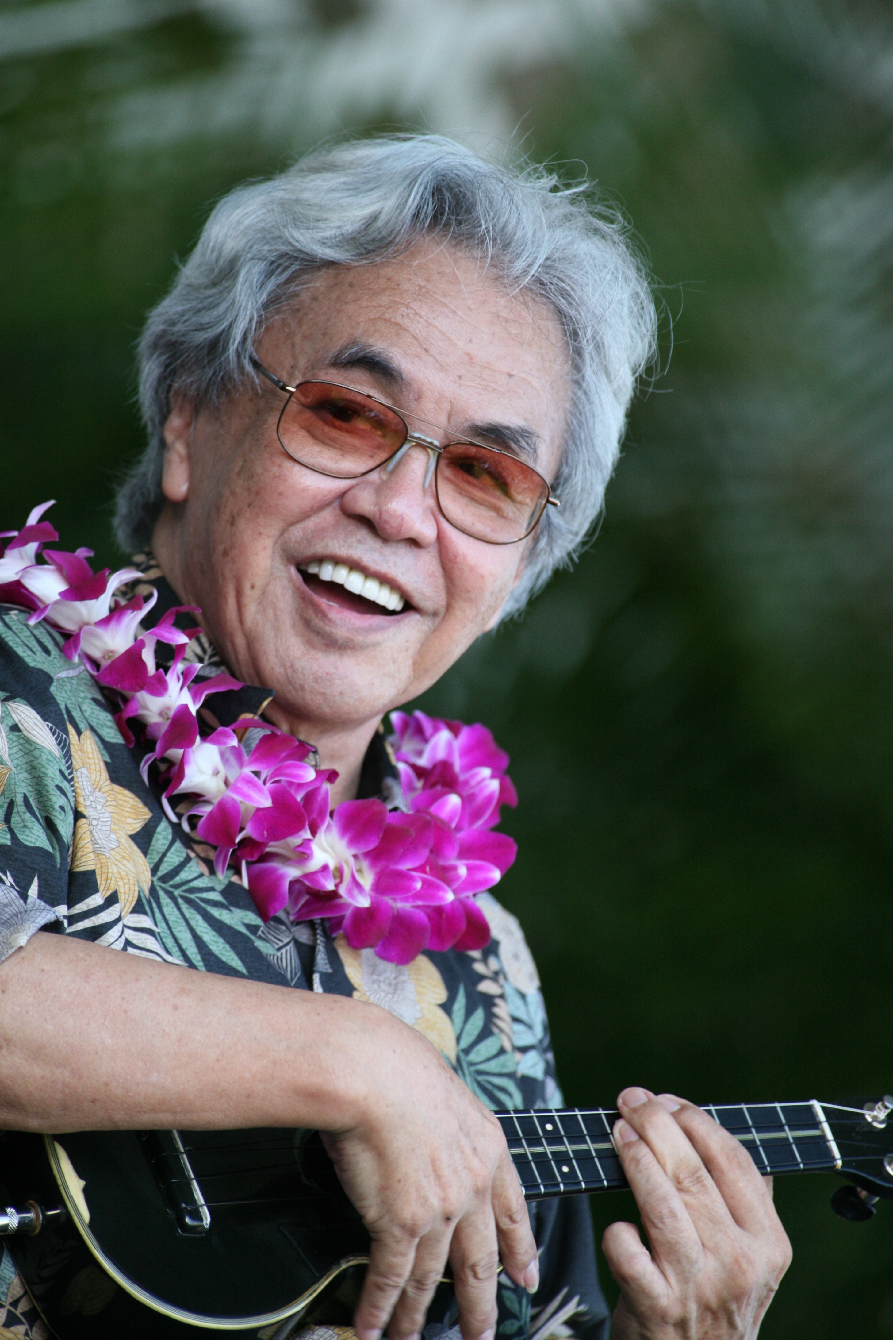 Man with gray hair and glasses playing a ukelele.