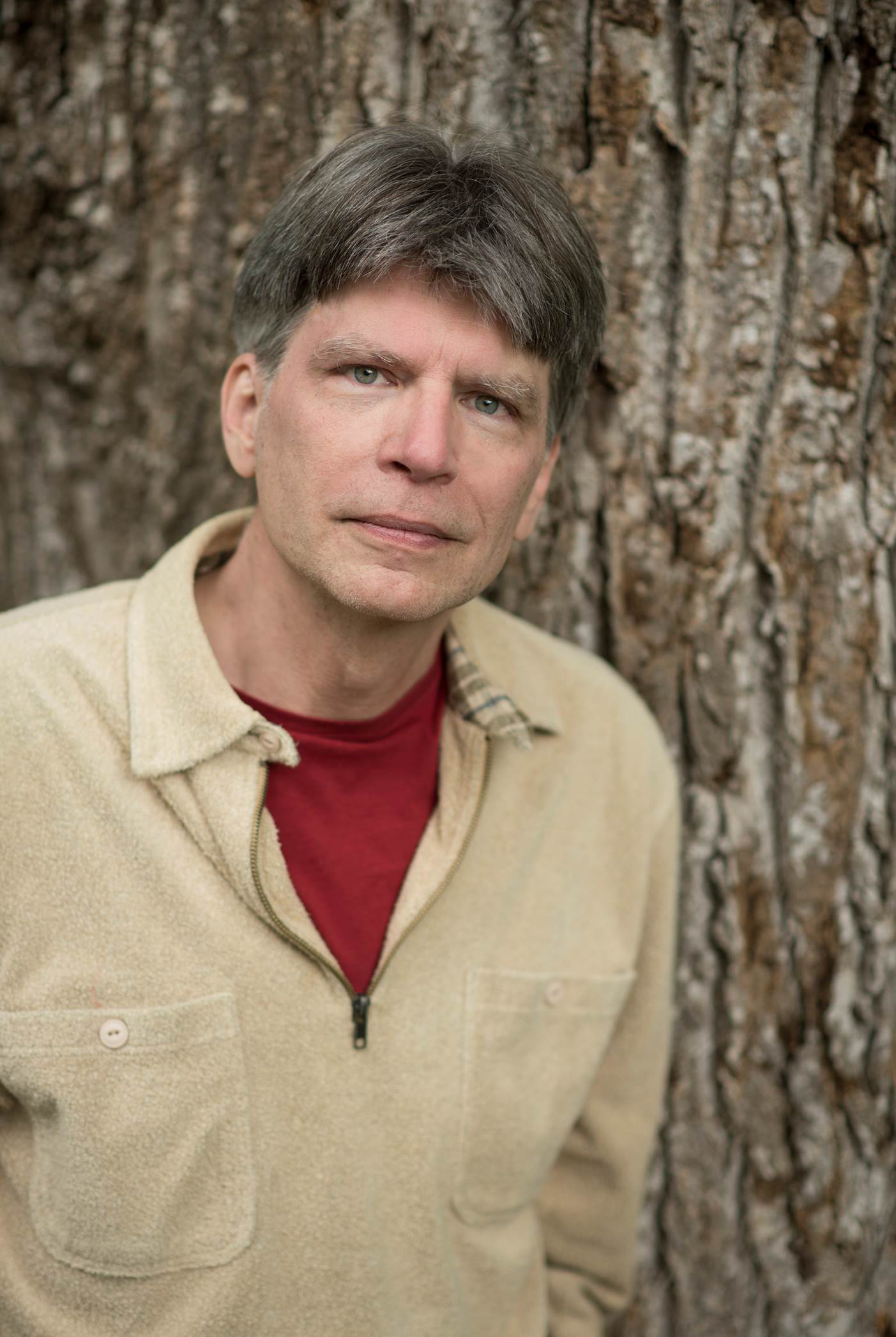 A man with light yellow shirt posting in front of a tree.