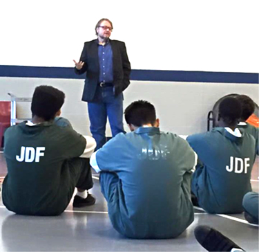 : Luis Alberto Urrea talks before a group of young men in Juvenile Detention Facility uniforms.