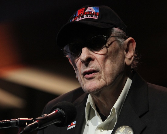 Close-up of NEA Jazz Master Joe Segal wearing a baseball cap and speaking into a microphone