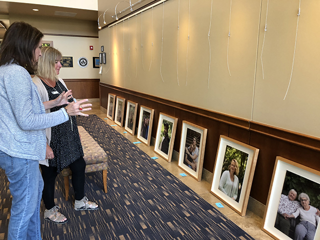 Two women look at and discuss framed photographs leaning against a wall before they are hung