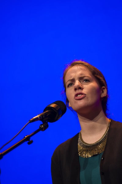 a young white woman reciting a poem on stage