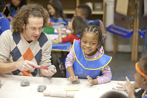 Artist and two young students working with clay at a table in the classroom