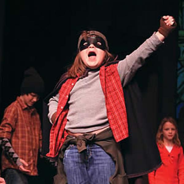 Cast of young actors, with one front and center with arm raised shouting something to the audience