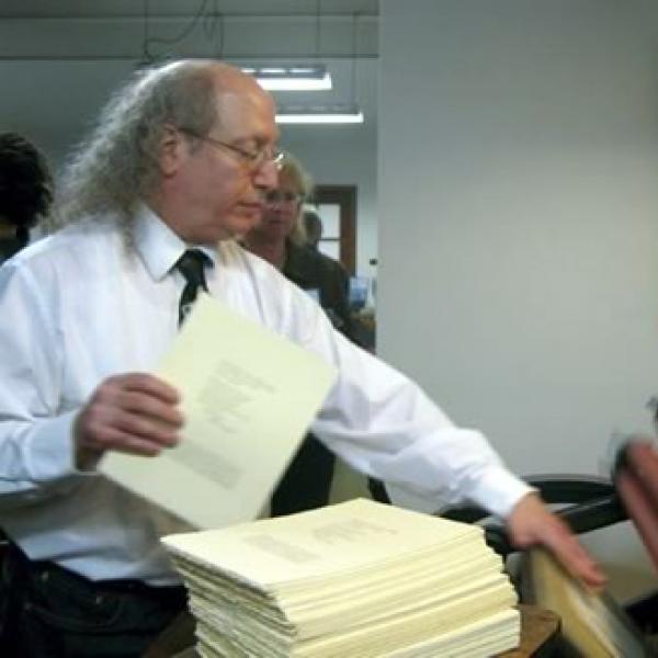 man at letterpress machine with a stack of broadsides in front of him? 