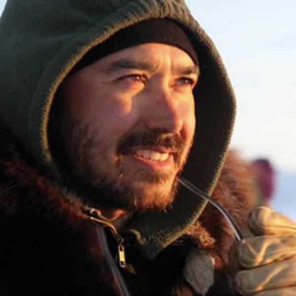 Photo of Andrew Okpeaha MacLean on location wearing winter coat and hood
