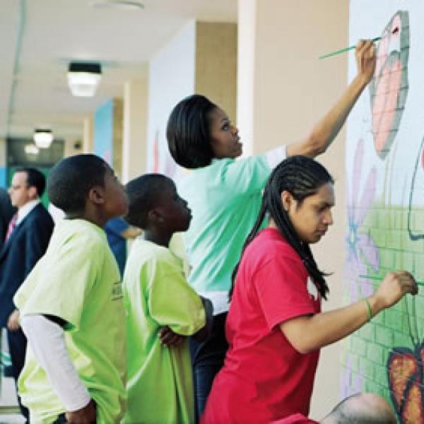 Michelle Obama and young African American students painting a mural on a brick wall
