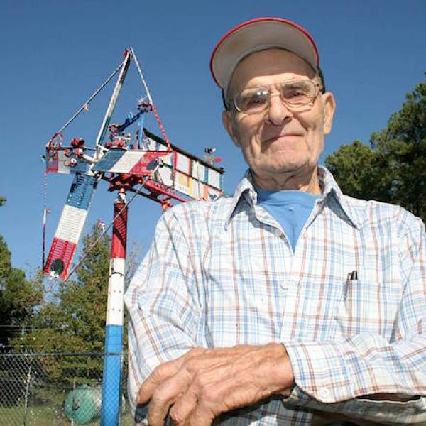 A man poses in front of a large pole topped by a scuplture.