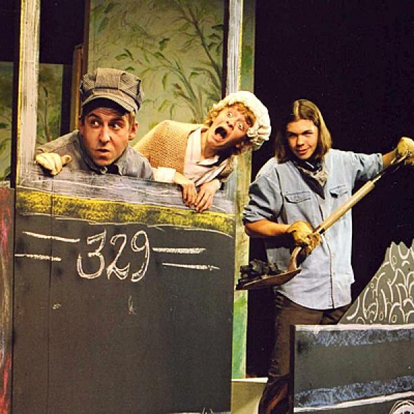 young actors in a cardboard locomotive mock-up with  another shoveling pretend coal into the firebox.