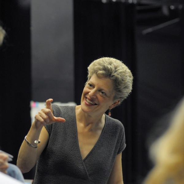 Woman gesturing to actors on stage. 