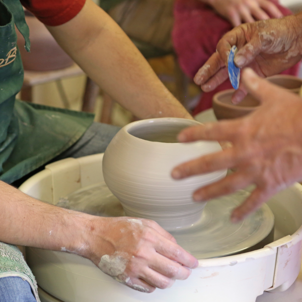 Arms and hands of people working on a pottery wheel