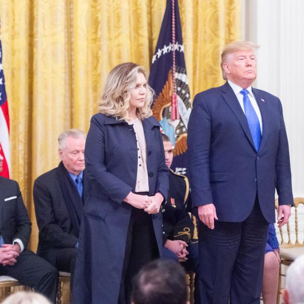 Woman in suit next to man in suit during ceremony. 