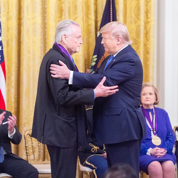 Two men in front of American flag embrace. 