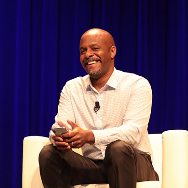 A man smiles while sitting in a chair and holding a phone