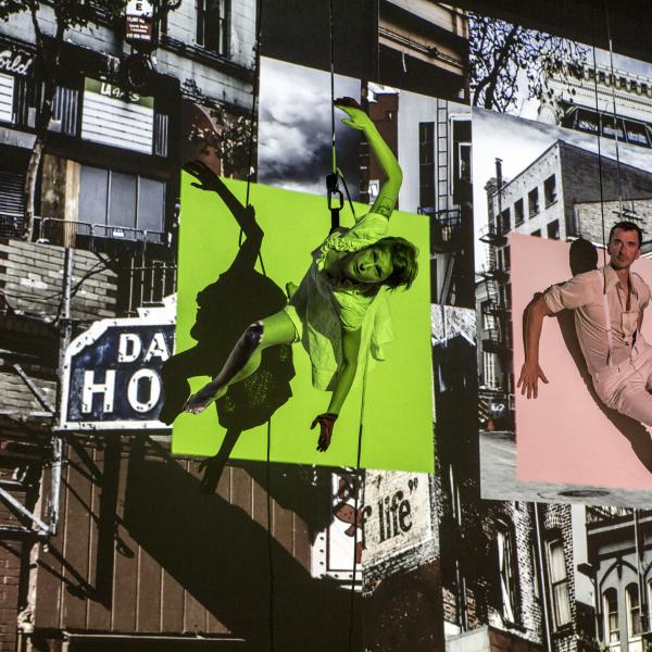 Two dancers suspended against a side of a building with video projections in the background