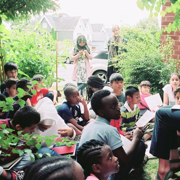 A woman shows students a worksheet while sitting in a garden