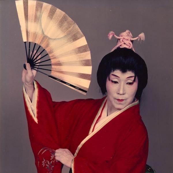 A female Japanese classical dancer in white face paint, a dark updo wig, holding a fan