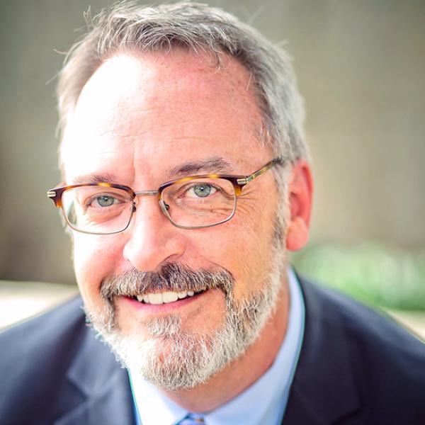 Headshot of a man smiling with glasses and gray hair