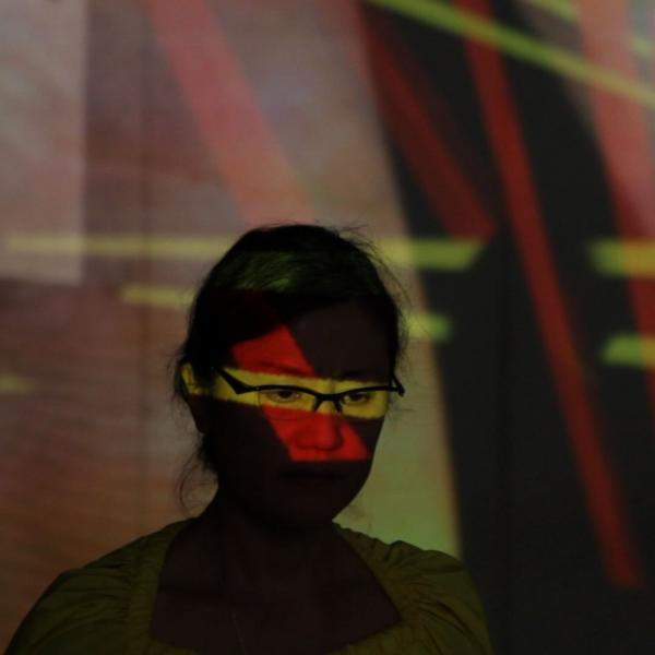 Woman in glasses with colored lights reflected on her.