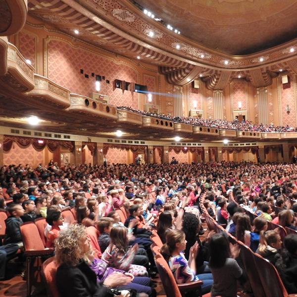 Young kids sitting in audience of performing center. 