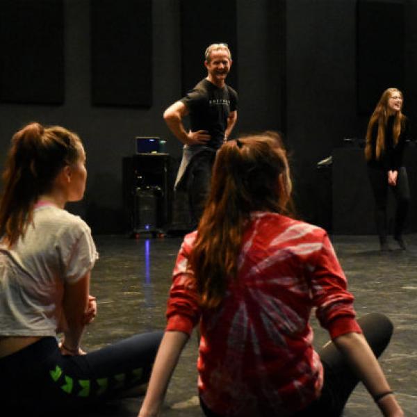 A laughing man stands in a circle of seated high school students