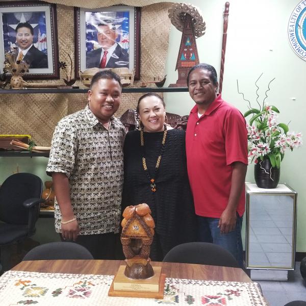 A woman stands between two men amidst cultural objects from the Northern Mariana Islands