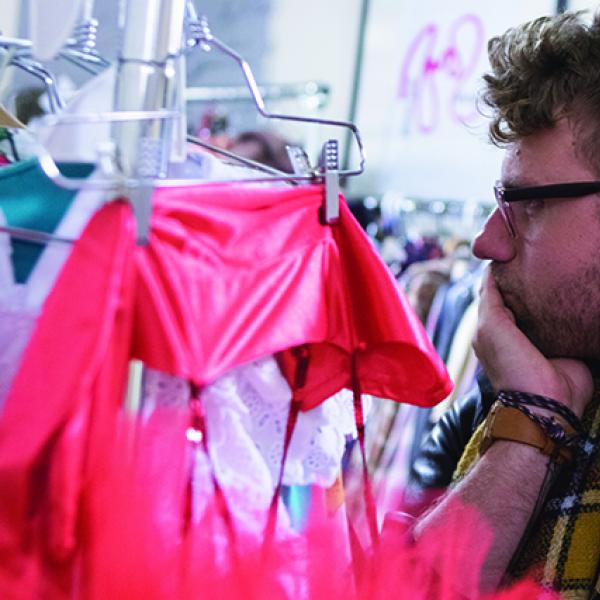 Man in scarf looking at clothes on hangers