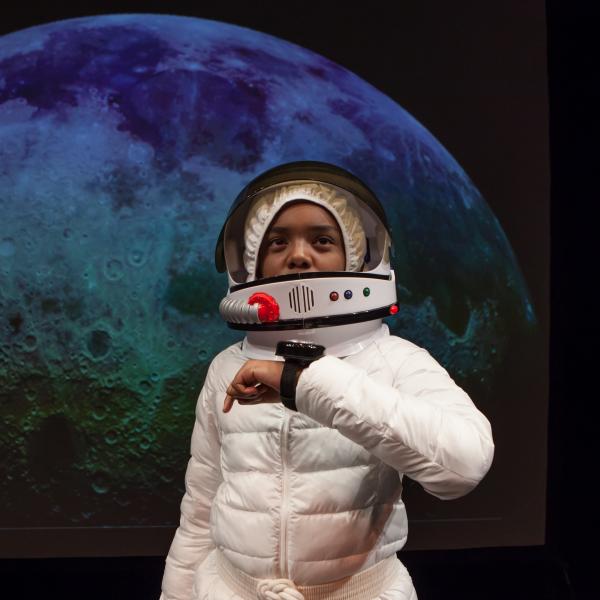 Boy in astronaut suit in front of photo of the moon. 