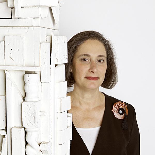 Woman wearing a black suit with large red brooch standing next to a white sculpture.