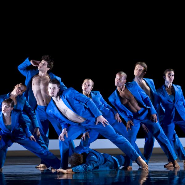 Six dancers dressed in blue on stage. 
